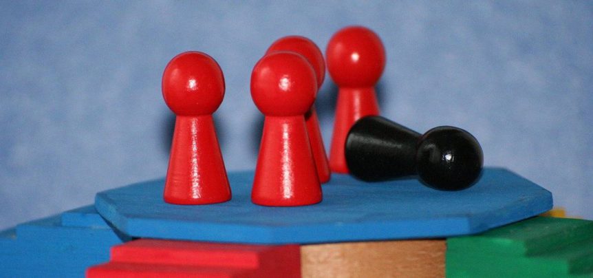 Several red wooden pieces representing people standing up, while a black piece is laying on the floor